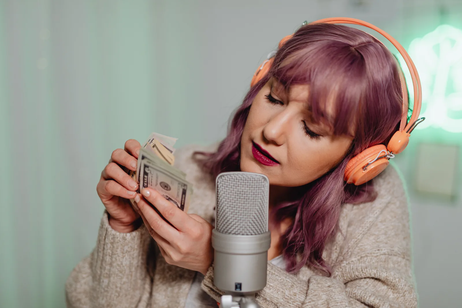 Woman wearing headphones recording ASMR with cash and microphone indoors. Livestream creator revenue metrics as practitioners see it