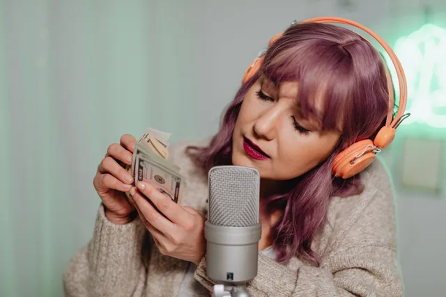 Woman wearing headphones recording ASMR with cash and microphone indoors. Livestream creator revenue metrics as practitioners see it